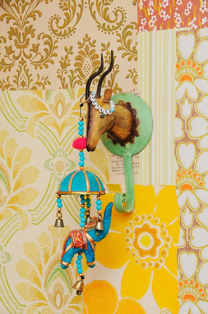 Retro ornaments in child's bedroom; Indian elephant mobile hanging from tin coat hook shaped like hunting trophy on patchwork of 70's wallpapers