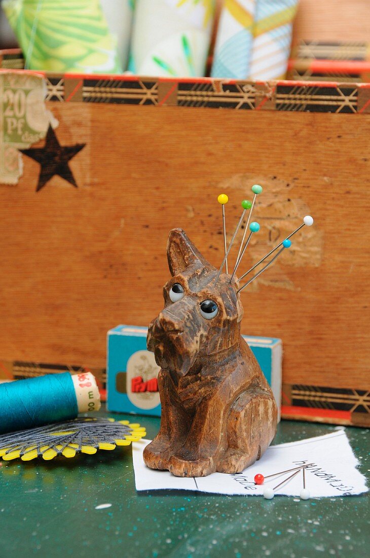 Sewing utensils and vintage, dog-shaped pincushion in front of sewing box made from old, upcycled cigar box