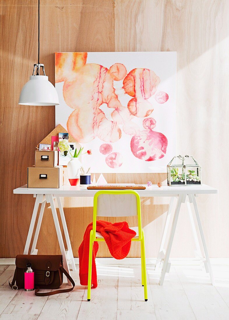 Weisser Arbeitstisch mit gelbem Stuhl; darüber ein abstraktes Aquarellbild
