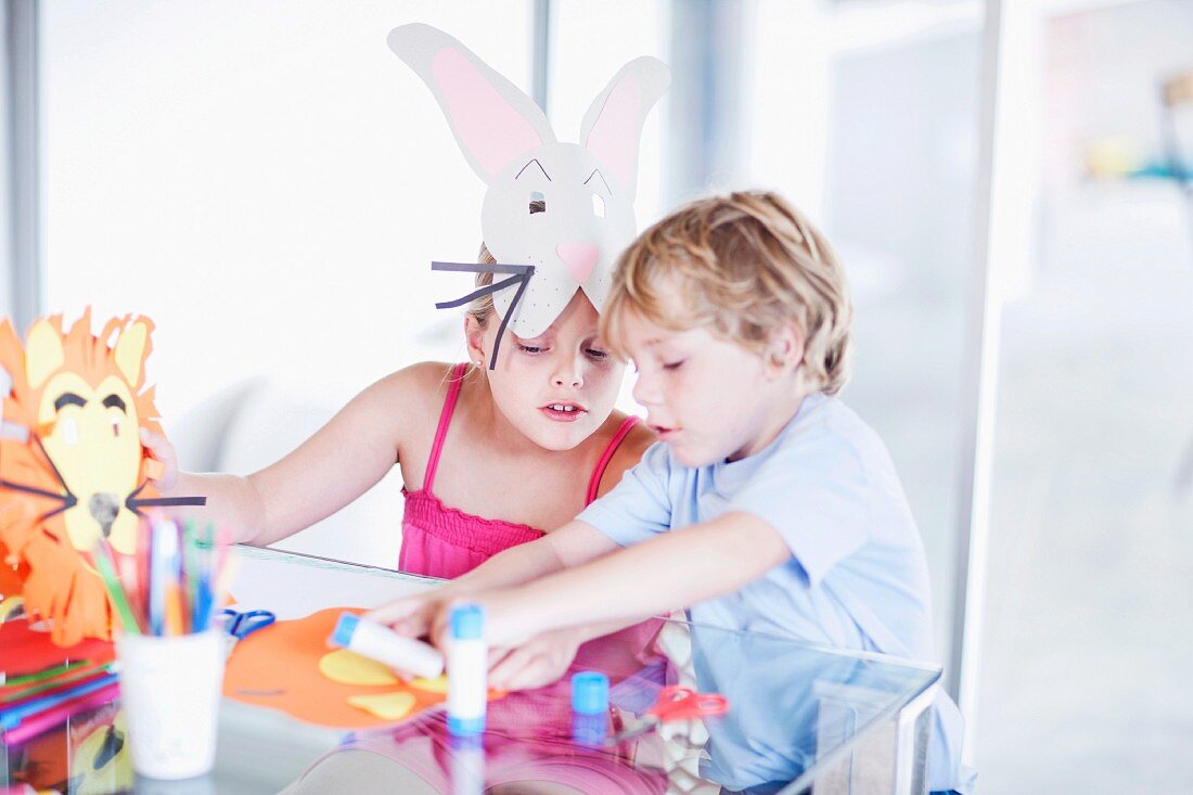 Two children making animal masks from coloured paper