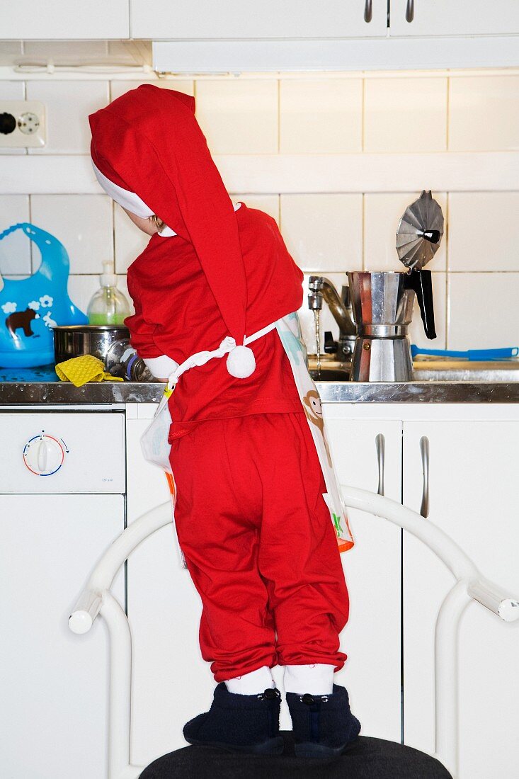 Kleiner Junge, als Weihnachtsmann verkleidet, wäscht Geschirr ab