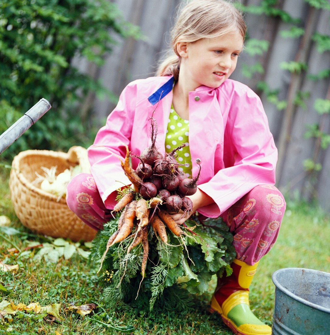 Mädchen hält einen Bund frisches Wurzelgemüse im Garten