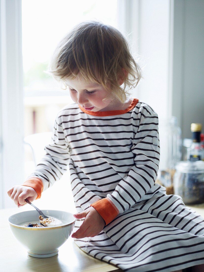 Kleines Mädchen isst Müsli auf einer Küchenarbeitsplatte