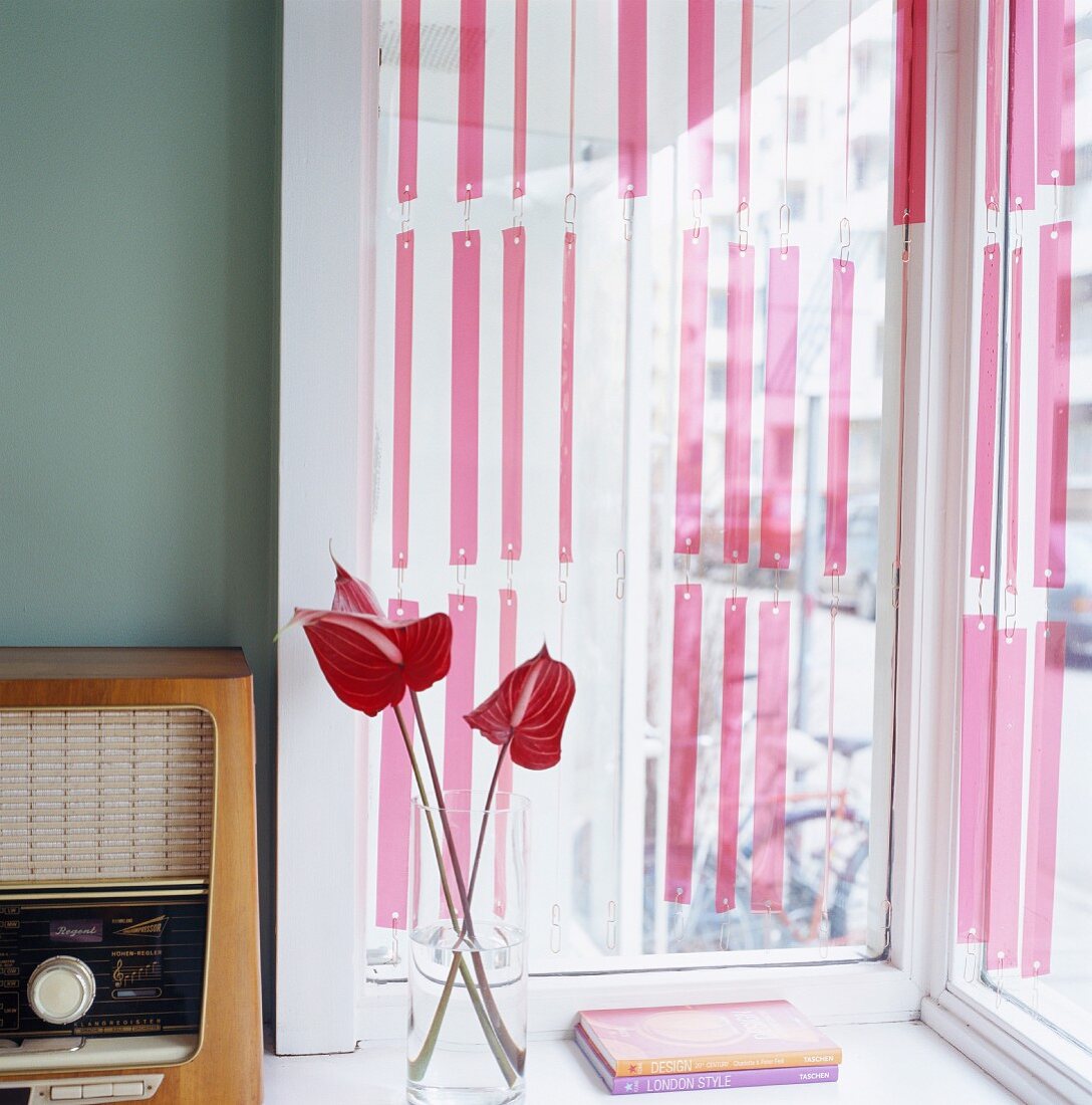 Vintage-Radio und Glasvase mit Flamingoblumen vor Fenster mit Streifenvorhang