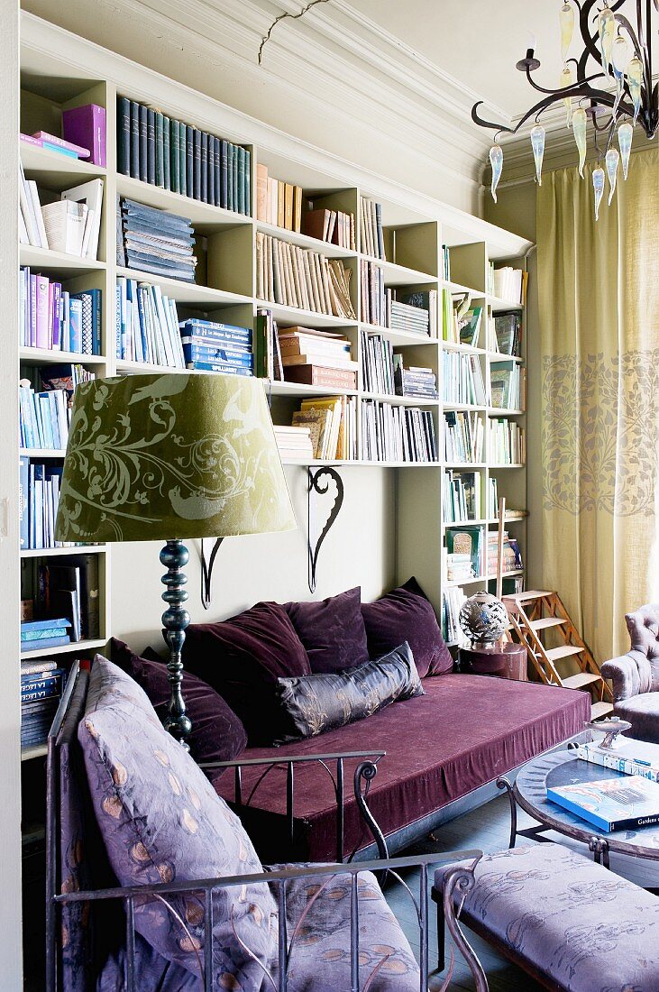 Wohnraum mit lila Couch & lila Sitzmöbeln vor Bücherwand
