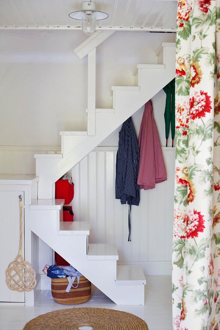 Blick neben Vorhang mit Blumenmuster auf weiße Treppe im Innenraum