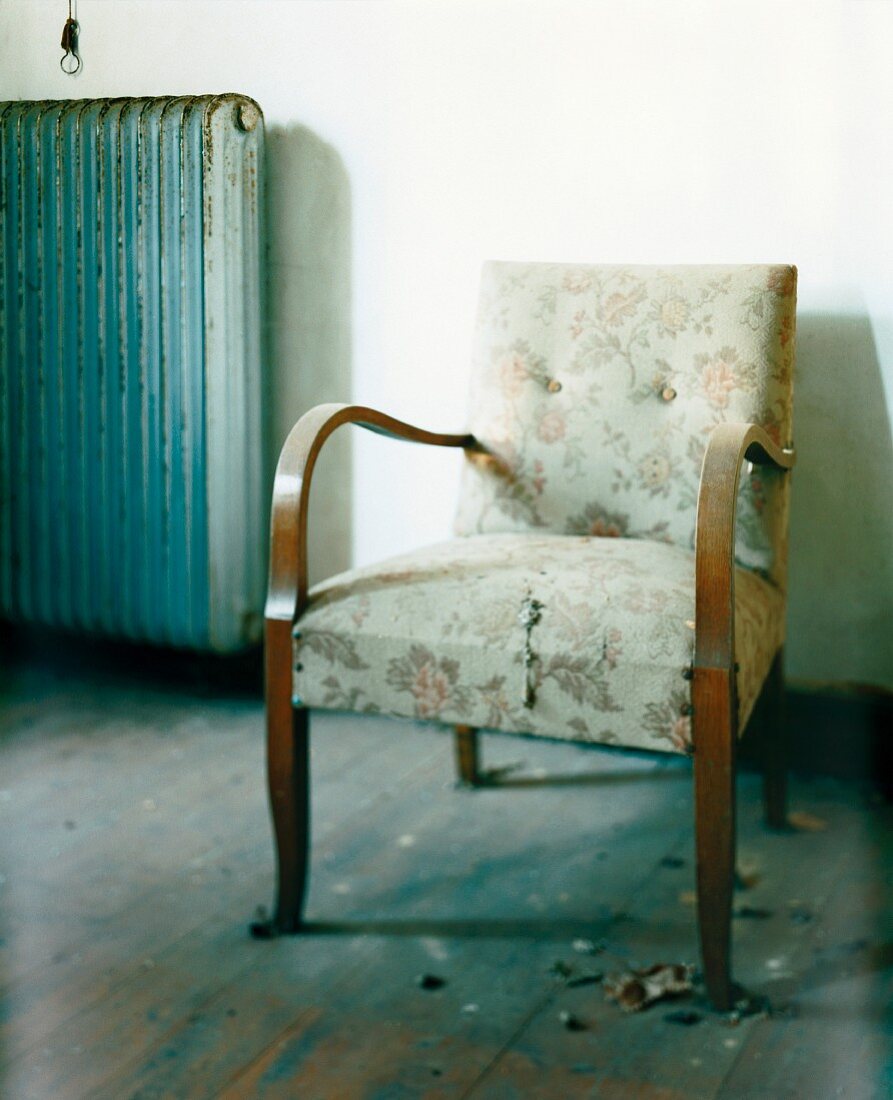 Biedermeier chair with torn upholstery and vintage radiator against wall