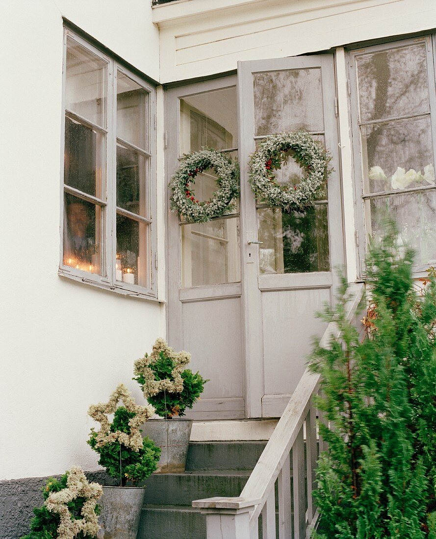 Blumentöpfe auf Treppenaufgang und aufgehängte Kranzdeko an Hintertür eines Hauses