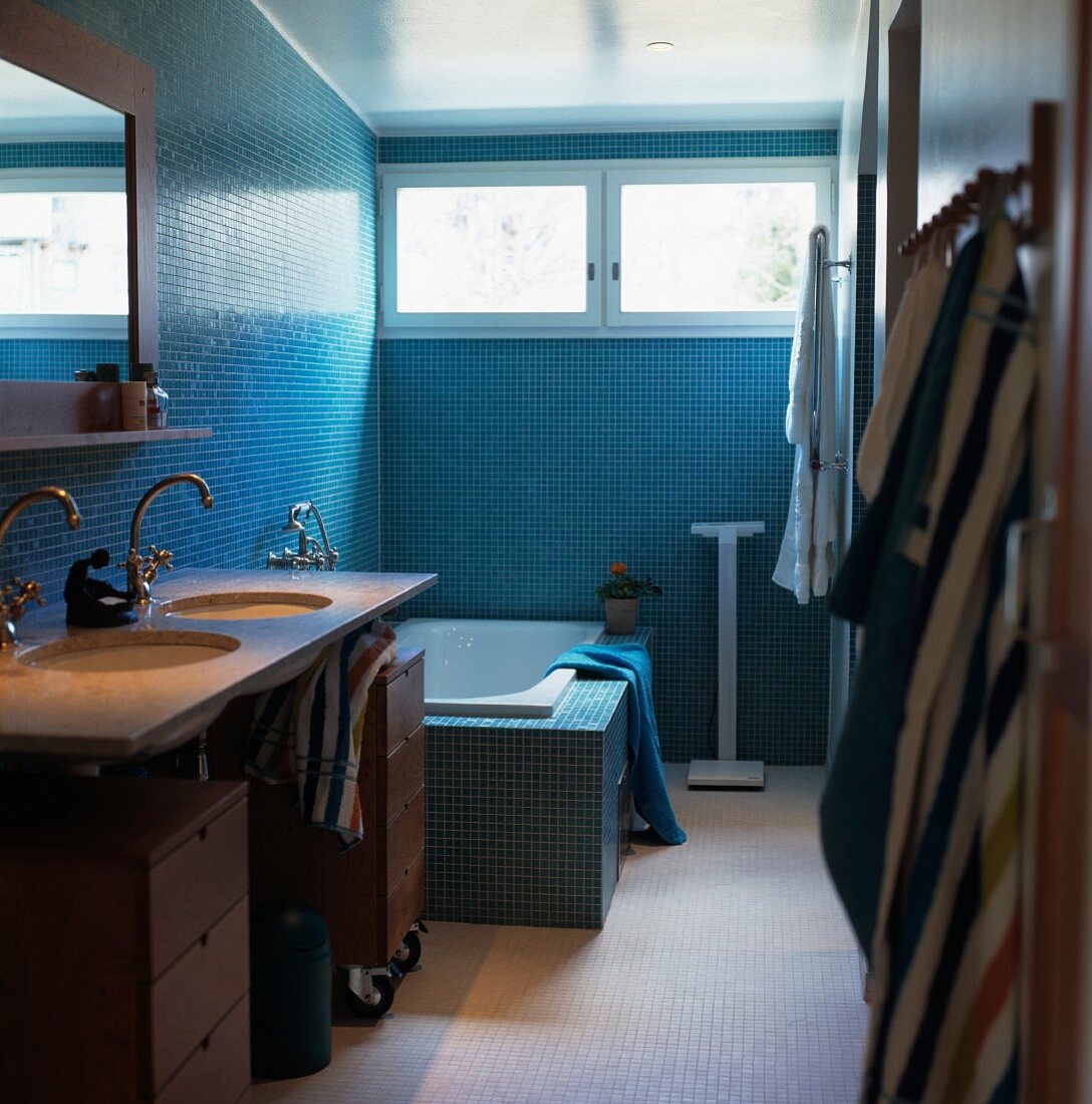 Bad mit Waschtisch und eingebauter Badewanne an Wand mit blauen Mosaikfliesen und Oberlicht