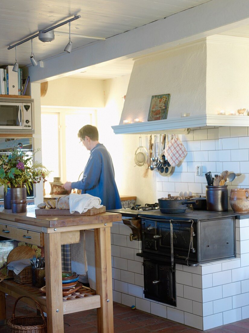 Frau in alter schwedischer Küche mit grossem Abzug über gemauerter Herdstelle