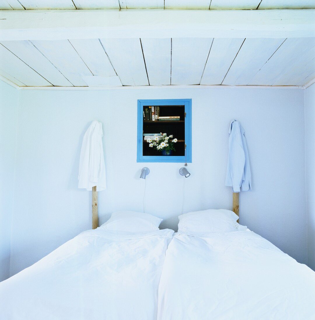 Einfacher rustikaler Schlafraum mit aufgehängten Hemden an hölzernen Bettpfosten beidseits einer blau gerahmten Wandnische
