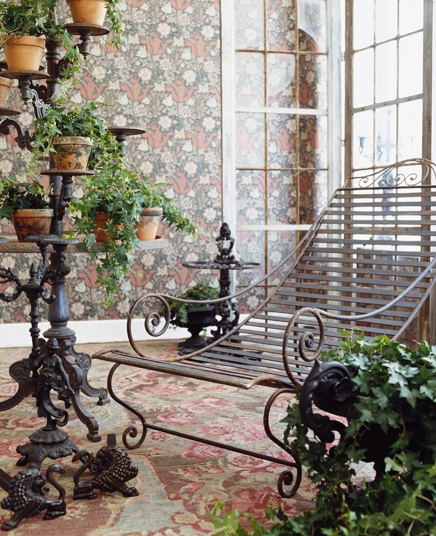 Liegestuhl und Wintergartendeko aus Eisen mit rankendem Efeu vor floralen Mustern auf Wand und Teppichboden