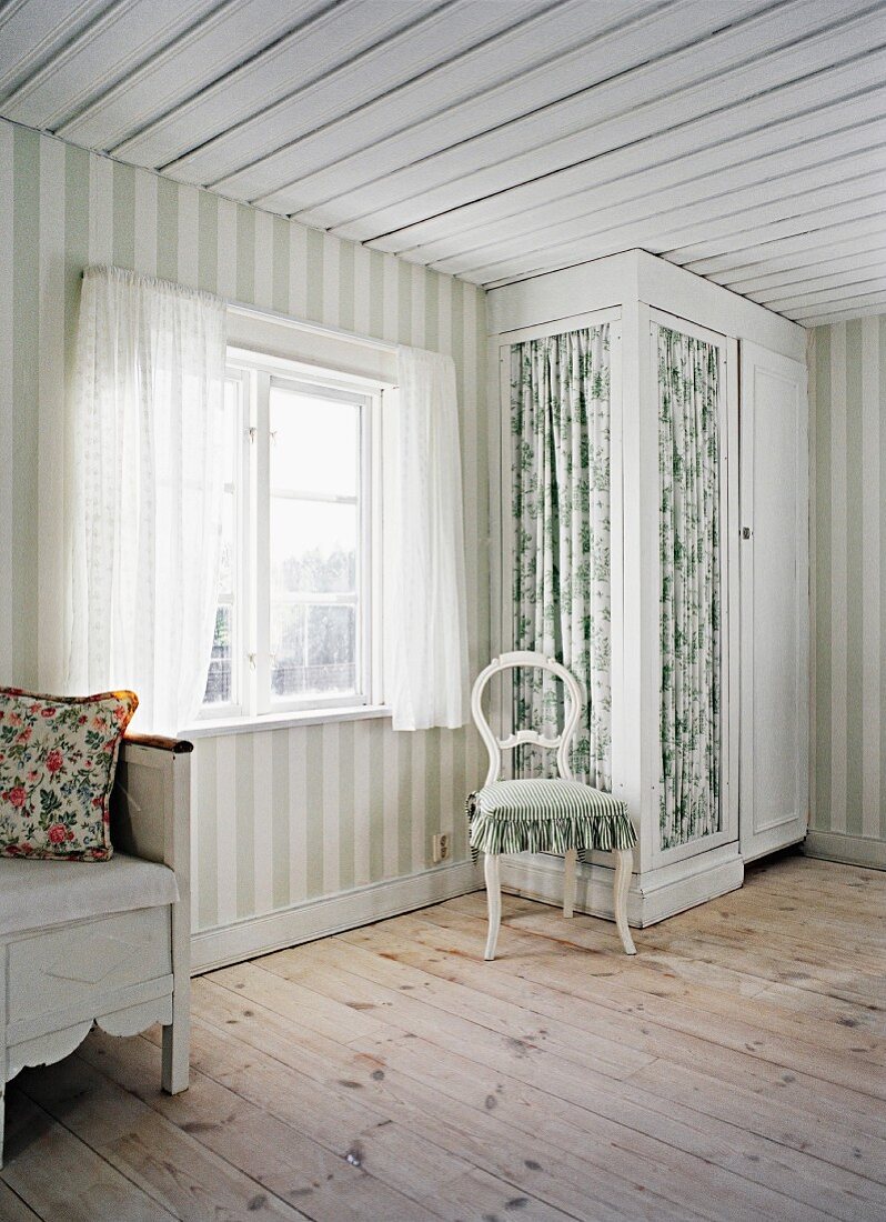 Heller Raum in skandinavischem Holzhaus mit Blockstreifen an der Wand und Einbauschrank mit geblümter Stoffbespannung