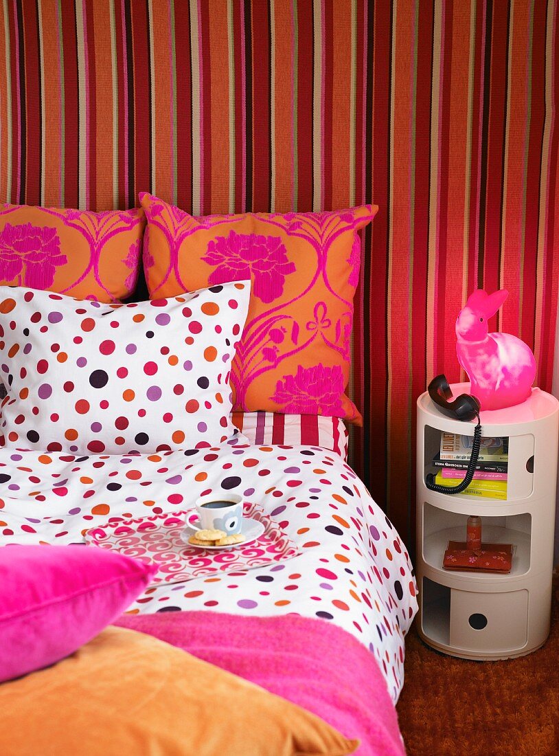 Coffee cup on tray and telephone on side table in bedroom; mixture of red and pink patterns on wall and bed linen