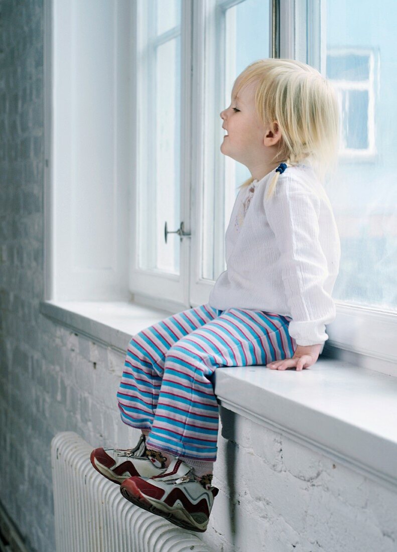 Kleines Mädchen sitzt auf Fensterbank