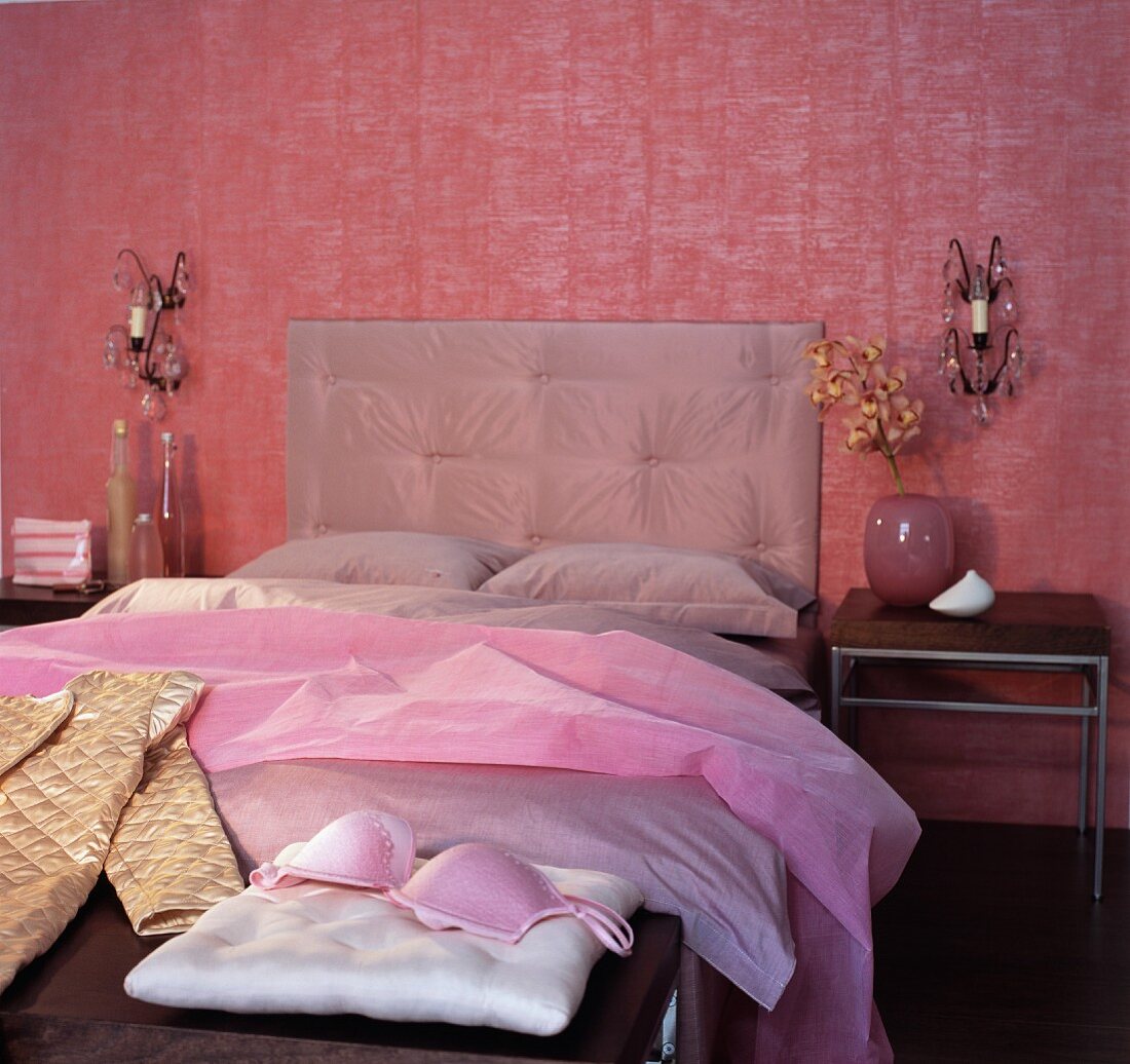 Elegantes Schlafzimmer in verschiedenen Rottönen mit Doppelbett und Damenwäsche auf Bank am Bettende