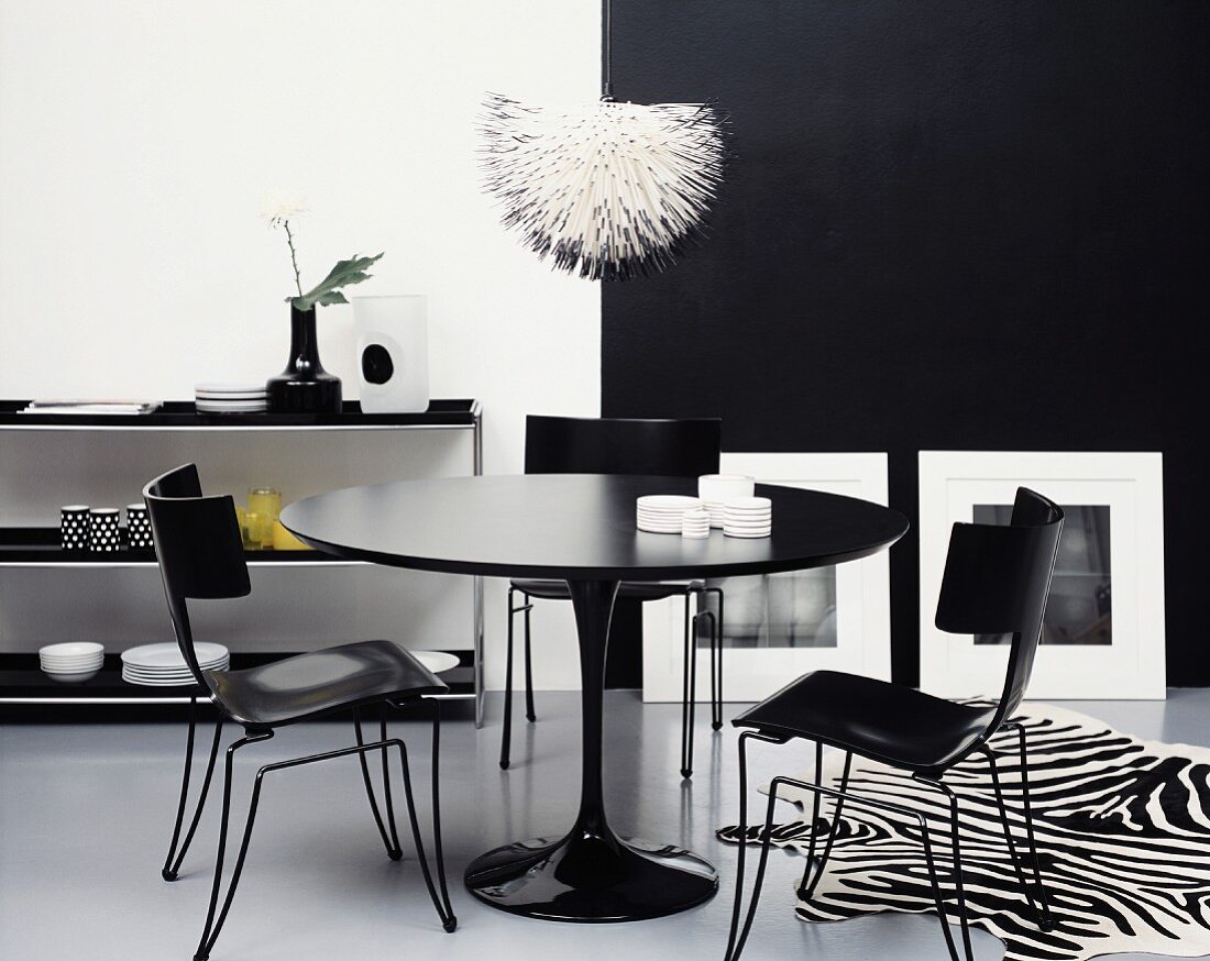 Schwarz-weisses Esszimmer: Runder Tisch und Stühle in Schwarz neben Zebrafell vor schwarz-weisser Wand