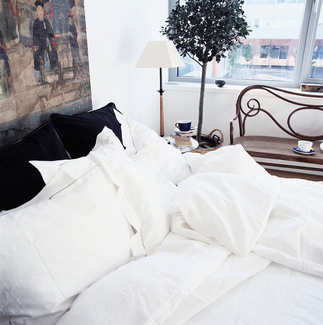 Bett mit weisser Bettwäsche und antike Sitzbank am Fenster