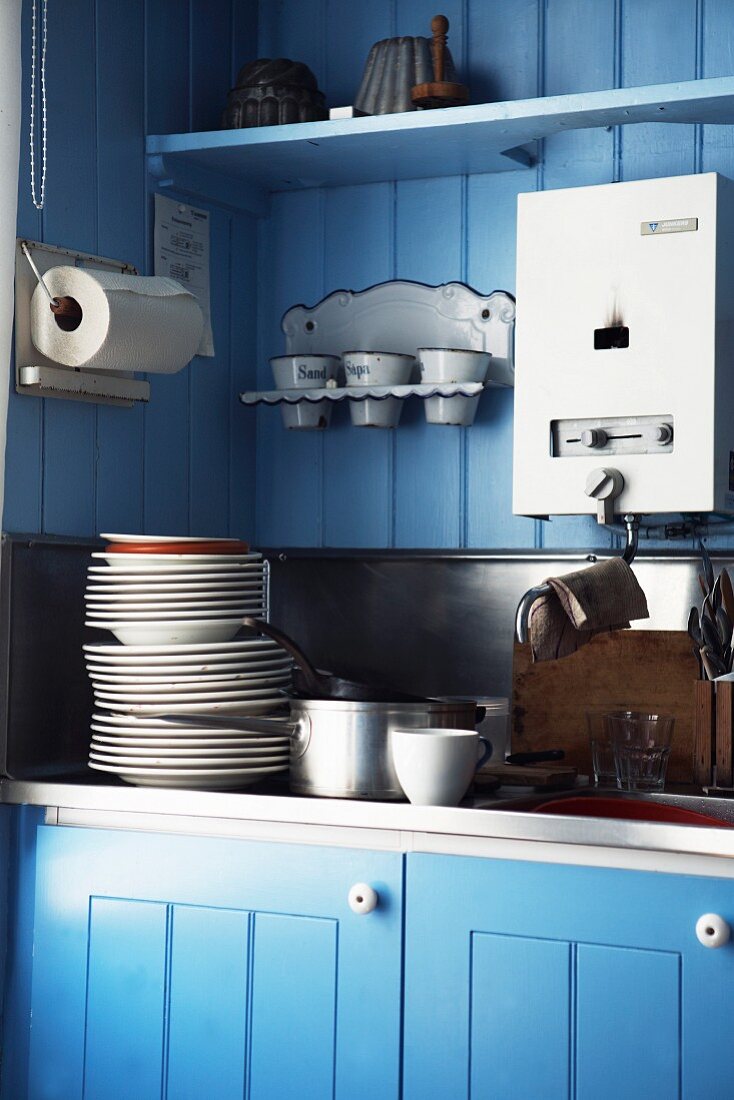 Ausschnitt einer Küchenspüle mit Tellerstapel vor blau lackierter Holzwand