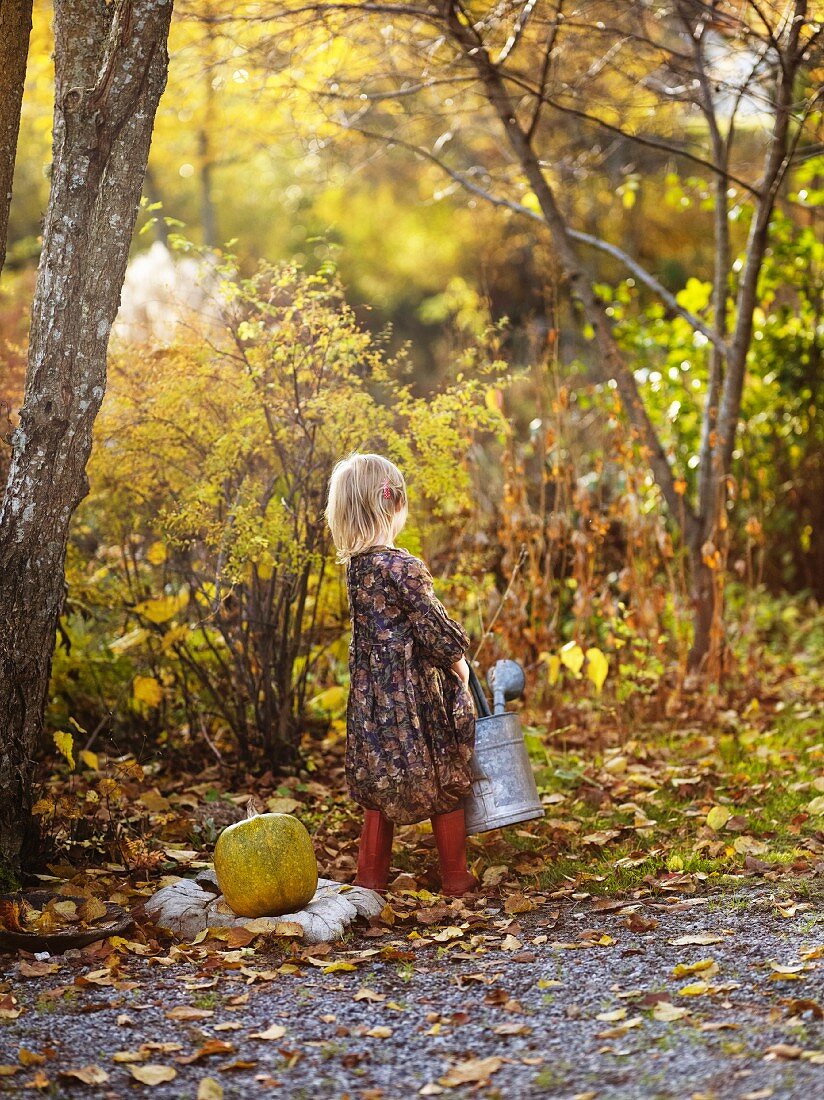 Kleines Mädchen mit Giesskanne im herbstlichen Garten