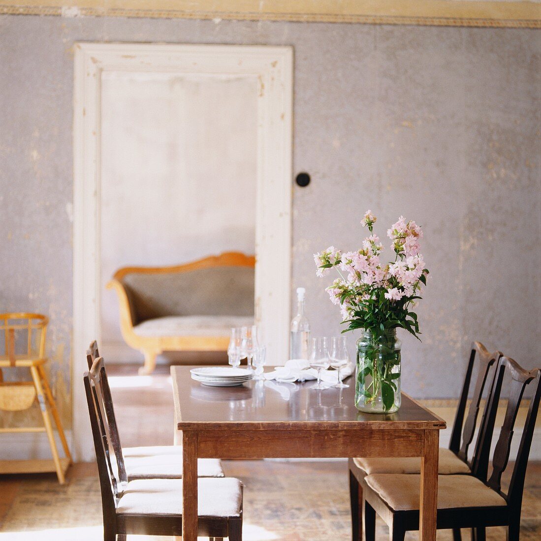 Blumenstrauss auf rustikalem Küchentisch und dunkle elegante Holzstühle vor Türöffnung in schlichtem Esszimmer