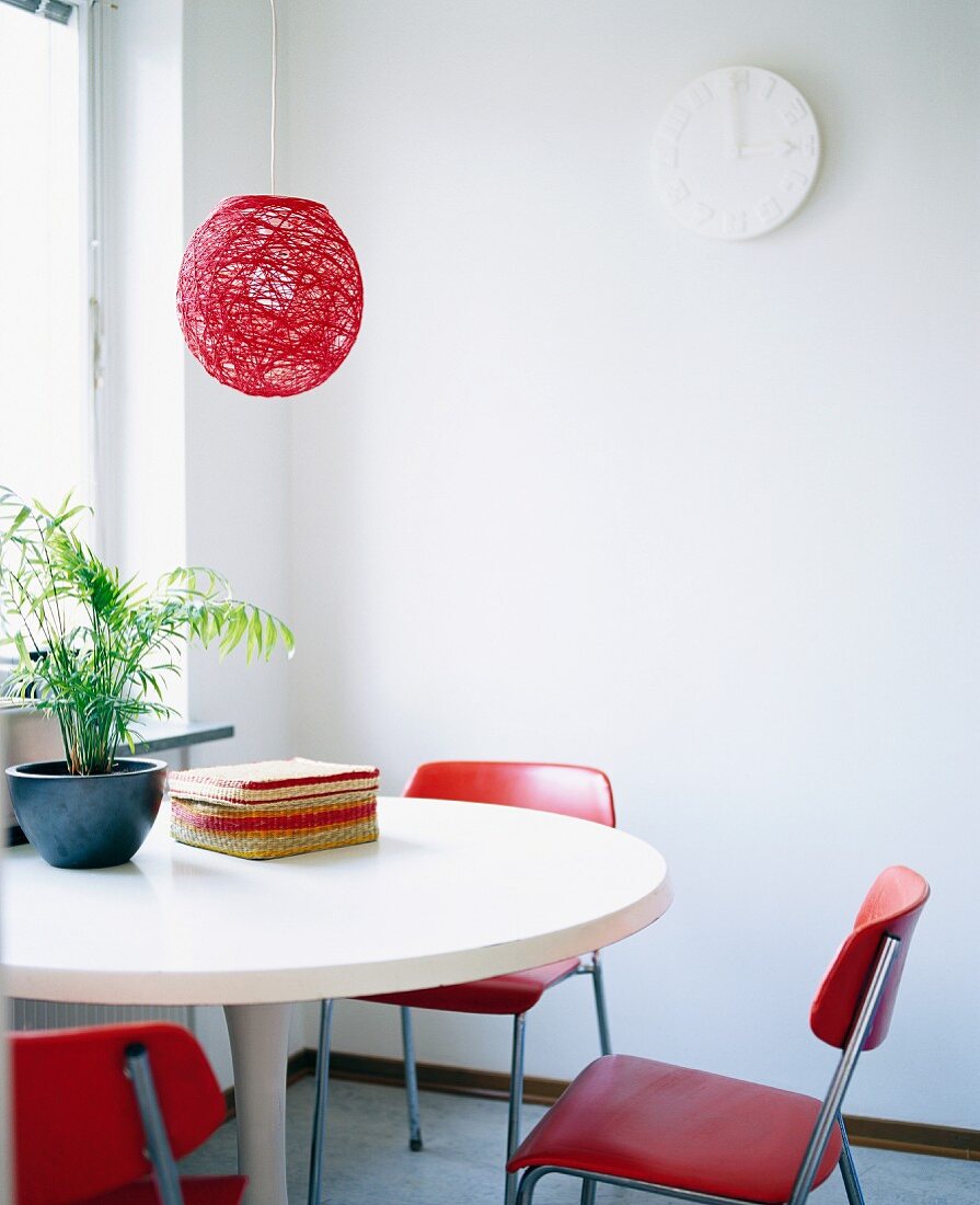 Rote Hängelampe über weißem Bauhaustisch mit roten Stühlen im Fiftiesstil
