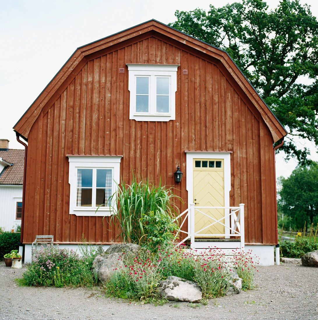 Traditionelles, skandinavisches Holzhaus mit Mansarddach und Vorgartengestaltung mit Findlingen