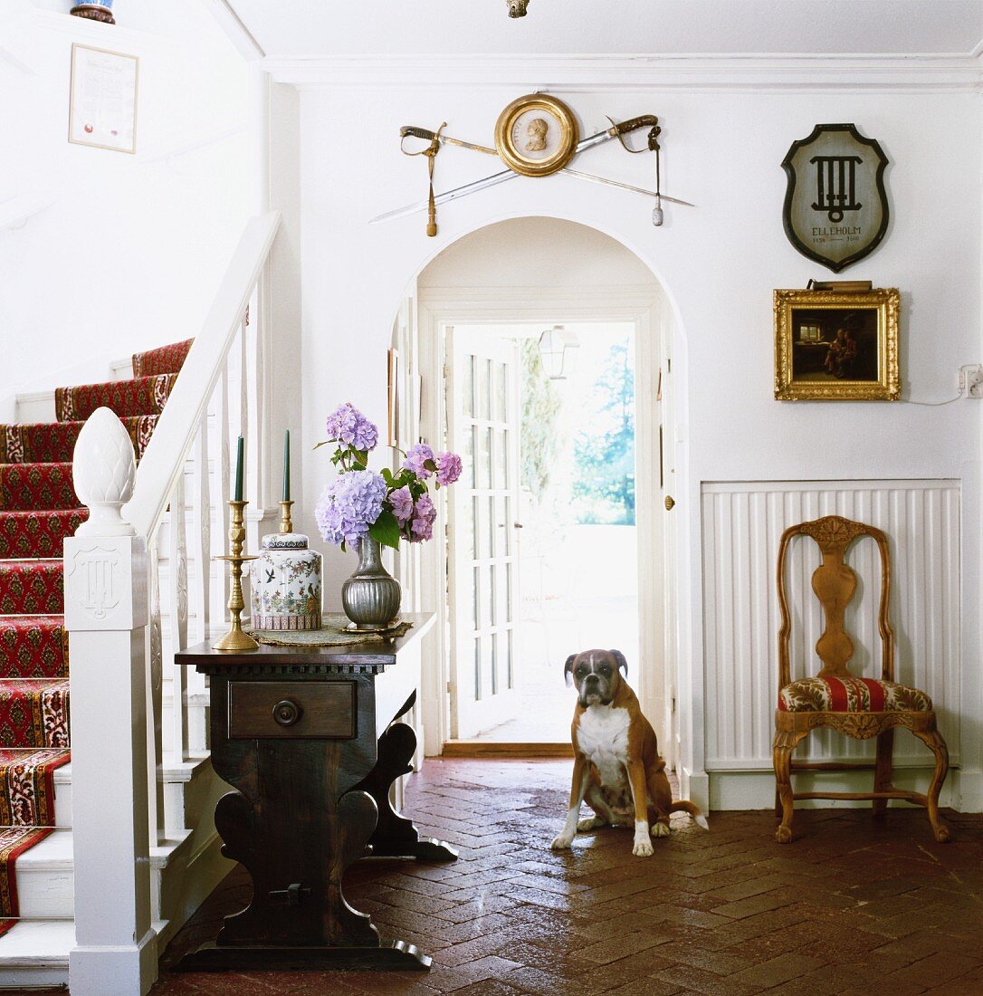 Diele mit Treppenaufgang in traditionellem schwedischem Holzhaus; Hund an der offenen Haustür