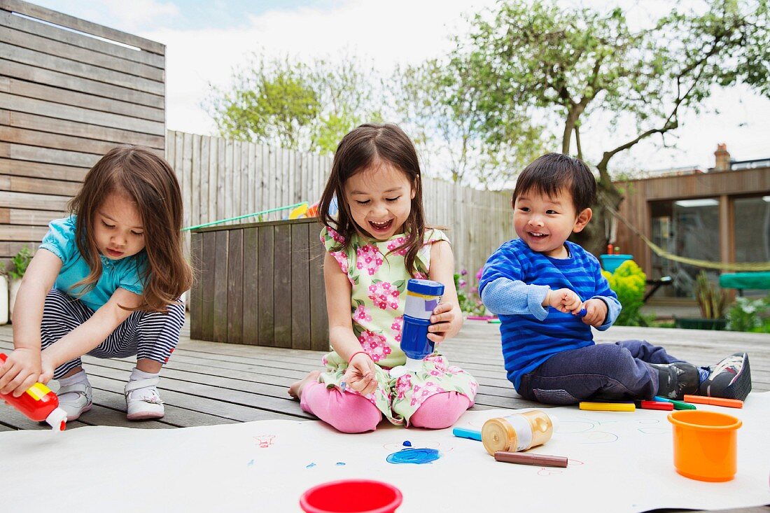 Kinder beim Malen im Freien auf Holzterrasse im Innenhof