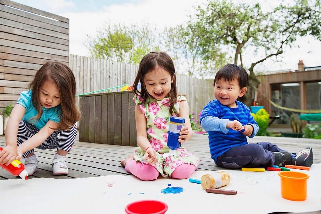 Three young children painting and drawing in garden