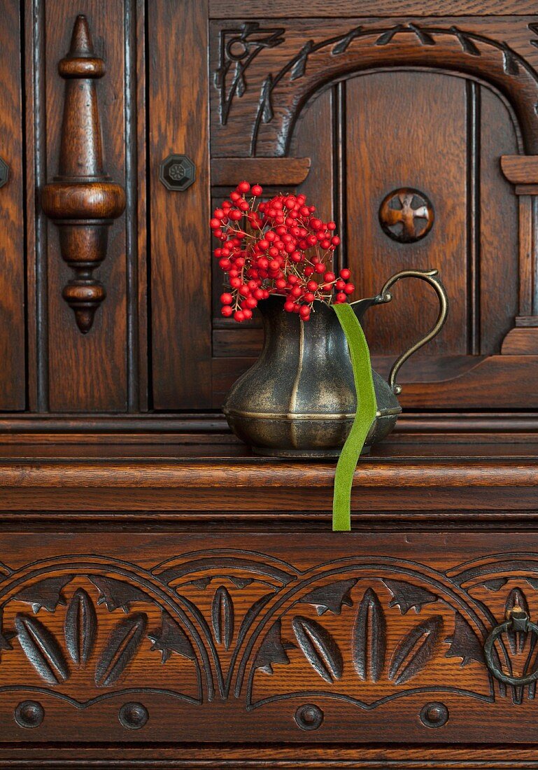 Rote Beeren in Vase aus Metall auf geschnitzter Kommode