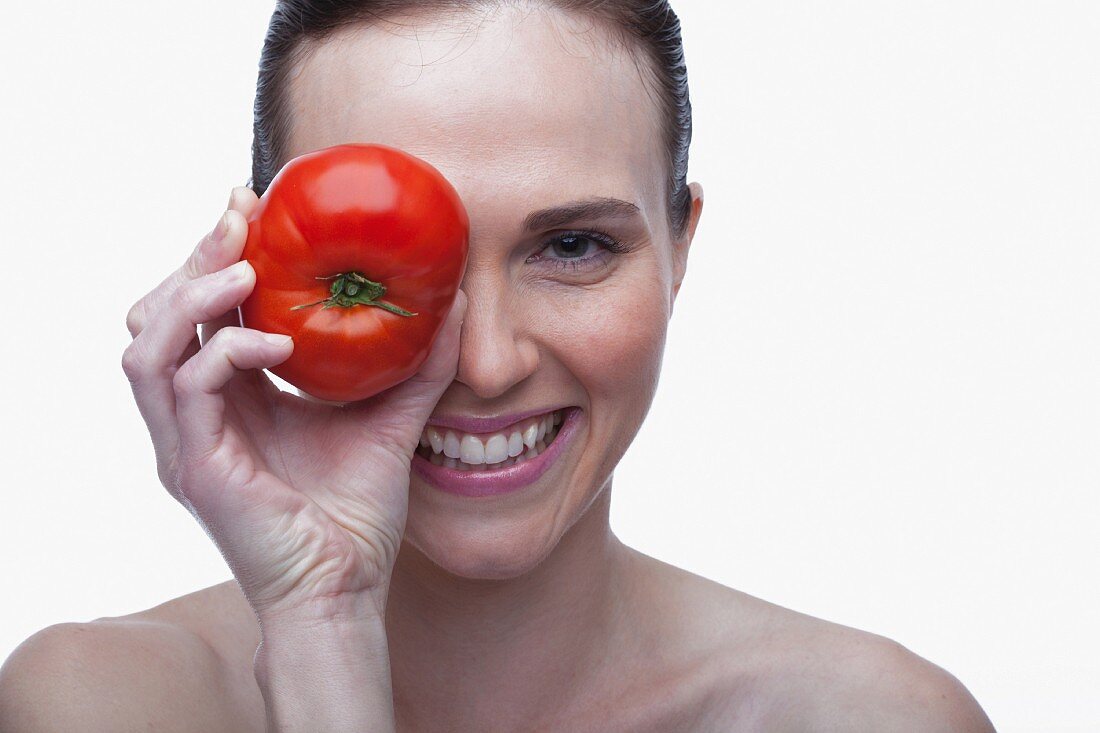 Young woman covering eye with red tomato