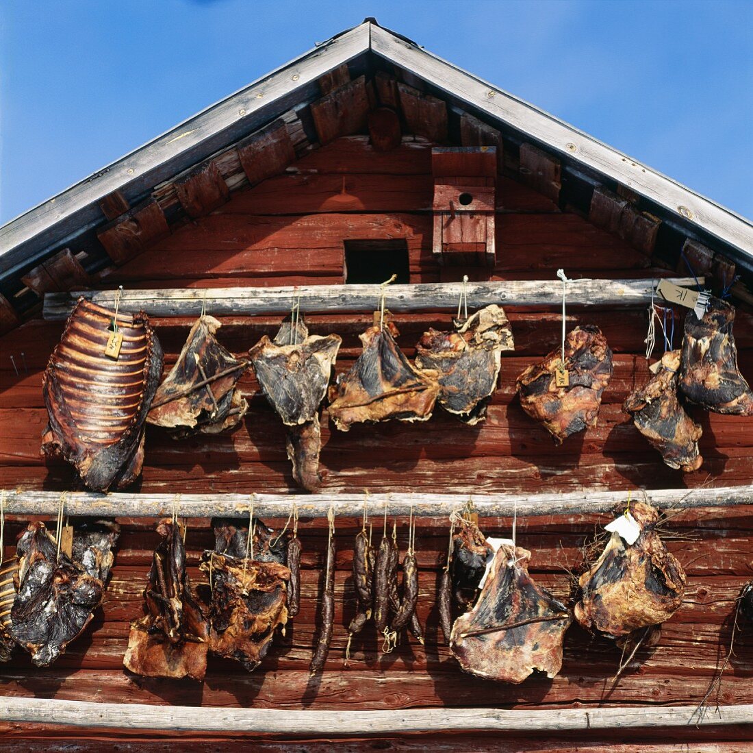 Aufgehängtes Rentierfleisch trocknet an der Aussenwand eines Holzhauses