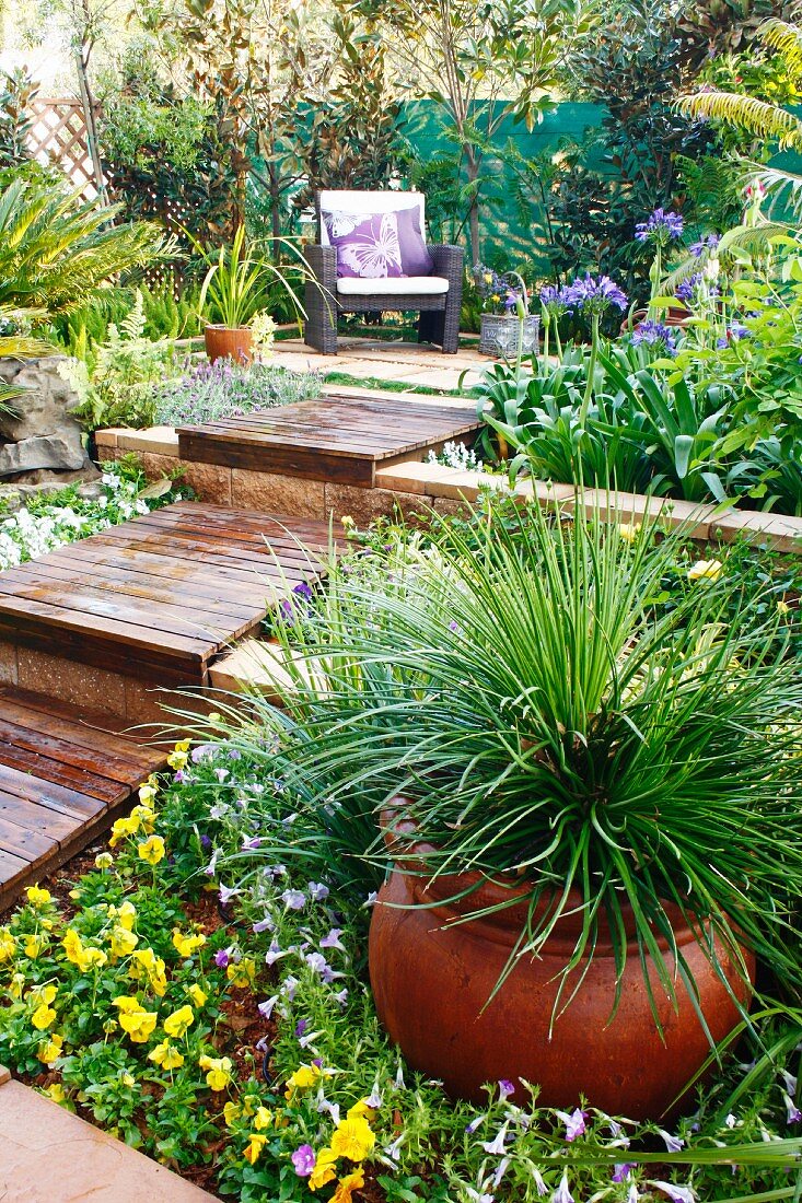 Kleiner terrassierter Garten mit gemütlichem Sitzplatz und grossem Tontopf mit Ziergras im Blumenbeet