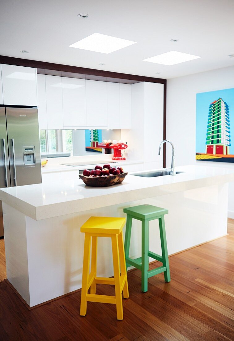 Farbige Holz Barhocker vor weisser Kücheninsel mit Spüle in offener Designer Küche