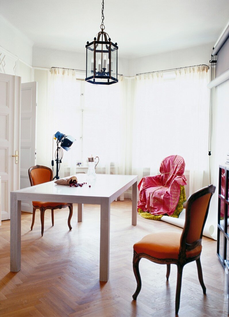 White table and antique chairs in grand interior with wrapped chair in bay window