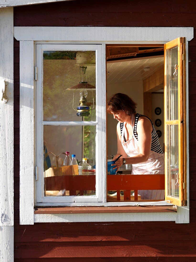 Blick durch geöffnetes Fenster auf Frau in der Küche