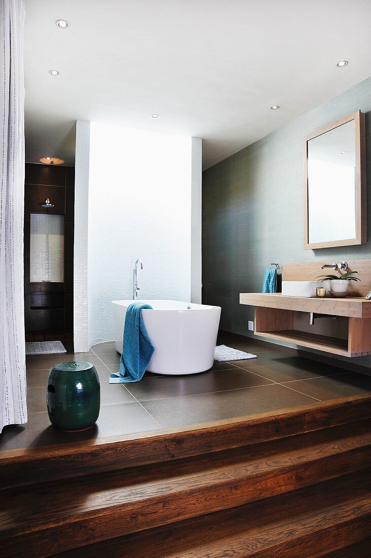 Freistehende Badewanne vor gebogener Wand in offenem Designerbad mit breiten Holzstufen