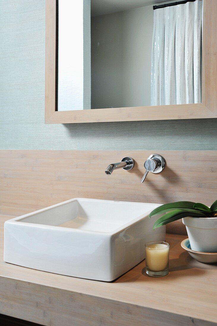 weiße Waschbecken auf Holzplatte vor Wandarmatur und gerahmtem Spiegel
