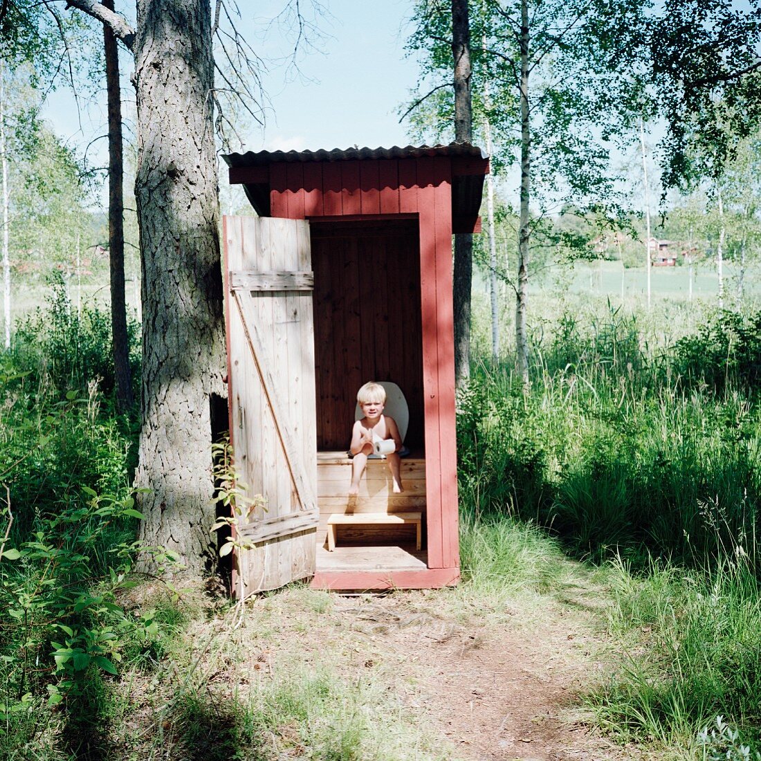 Little boy sitting on outhouse toilet
