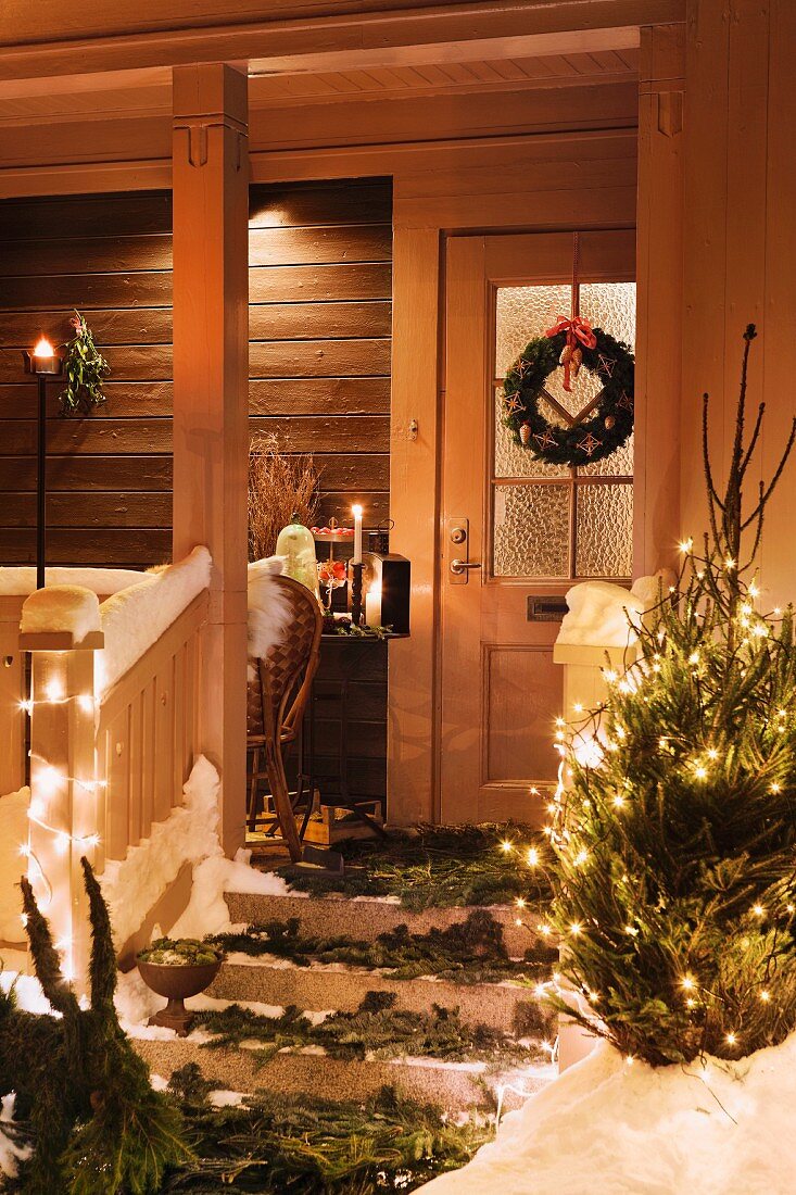 Front door and porch festively decorated with fir branches, door wreath & Christmas tree