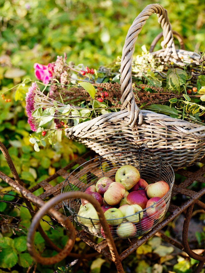 Apples and flowers in baskets on metal garden table