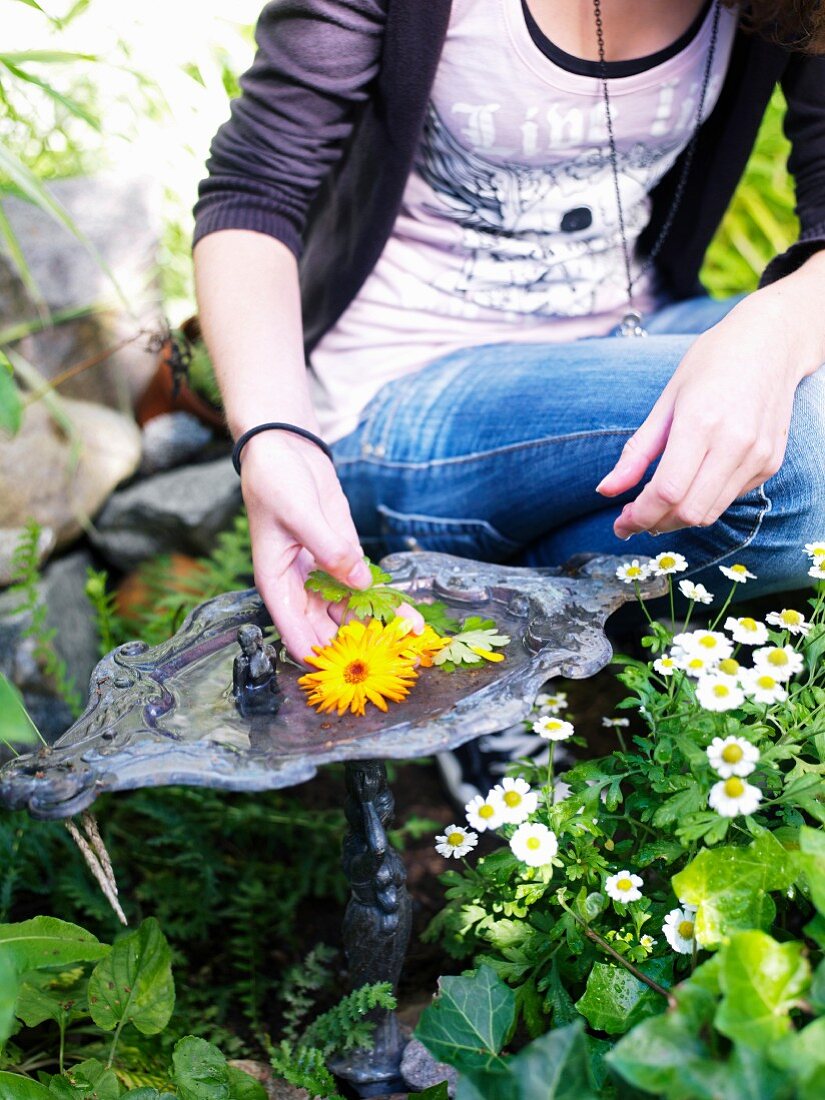 Junges Mädchen schmückt ein Vogelbad mit bunten Gartenblumen