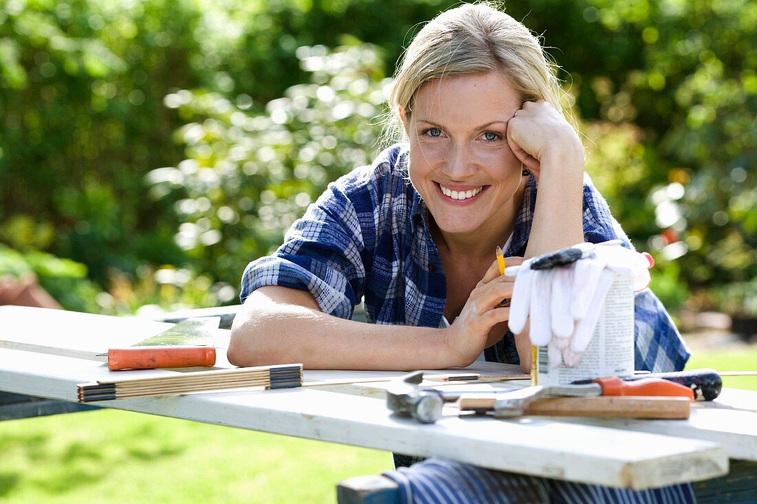 Frau lächelnd über provisorischen Handwerkertisch im Garten gebeugt
