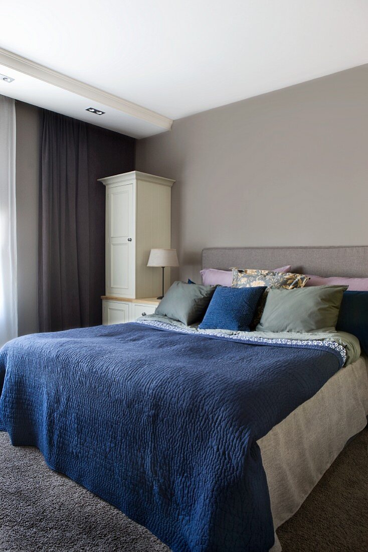 Double bed with blue bedspread in bedroom painted pale grey