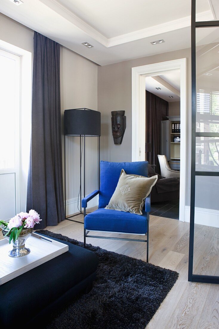 Tablett mit Blumenstrauss auf gepolstertem Couchtisch und blauer Sessel in Loungebereich, in der Ecke eine Stehleuchte