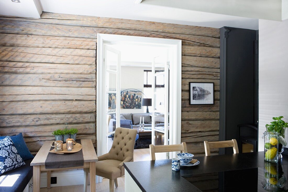 Black worksurface in front of dining area against rustic wooden wall and open double doors with view into living room
