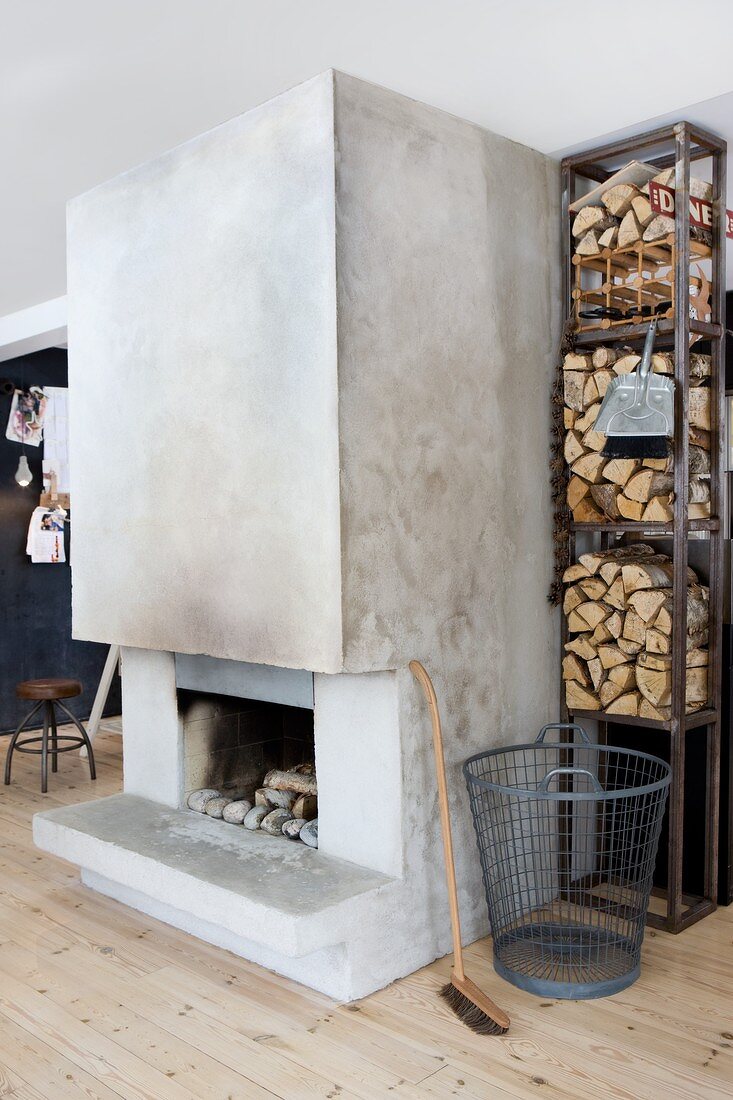 Stahlregal mit Brennholz und Betonkamin mit offener Feuerstelle in skandinavischem Wohnzimmer, Boden mit hellen Fichtendielen