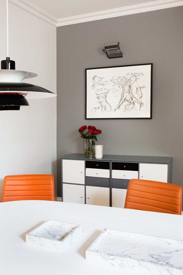 Teilweise sichtbare Poulsen Pendelleuchte über weißem Esstisch und Stühle mit Lederbezug vor Sideboard an grau getönter Wand