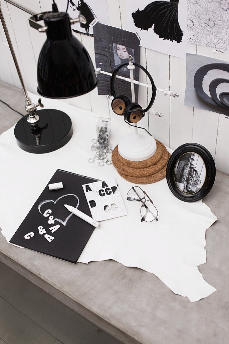 Kartengestaltung mit Klebebuchstaben, Kopfhörer und Vintageleuchte auf Schreibtisch im Betonlook; Modebildchen an weiss lackierter Wandverkleidung